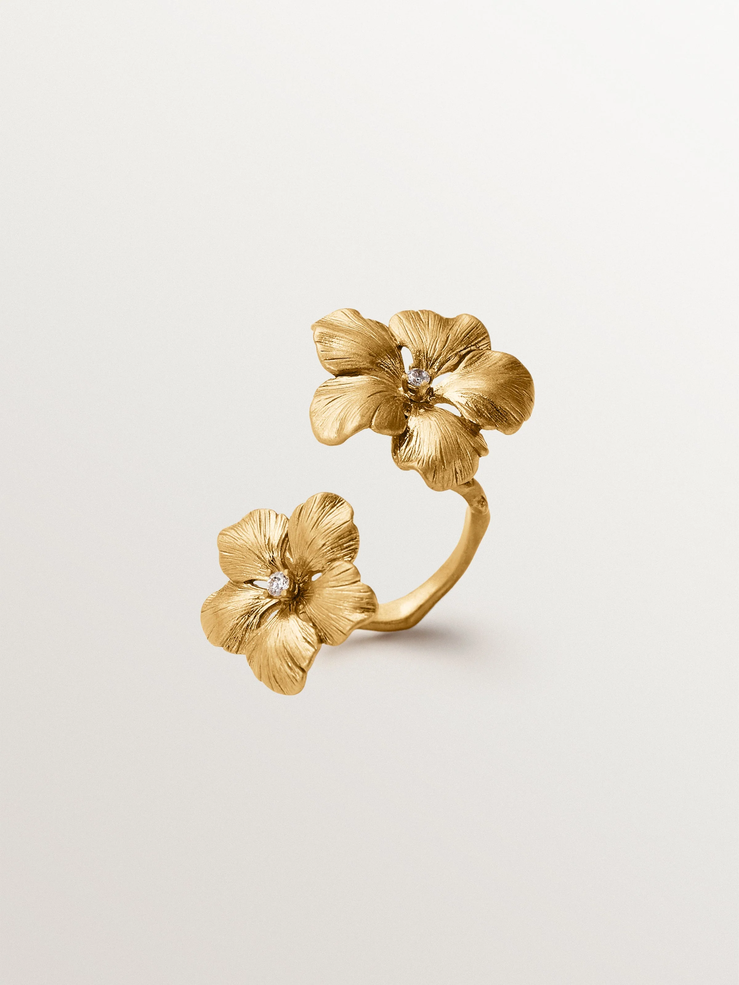 Anillo abierto bañado en oro amarillo con cristales y motivo de flor